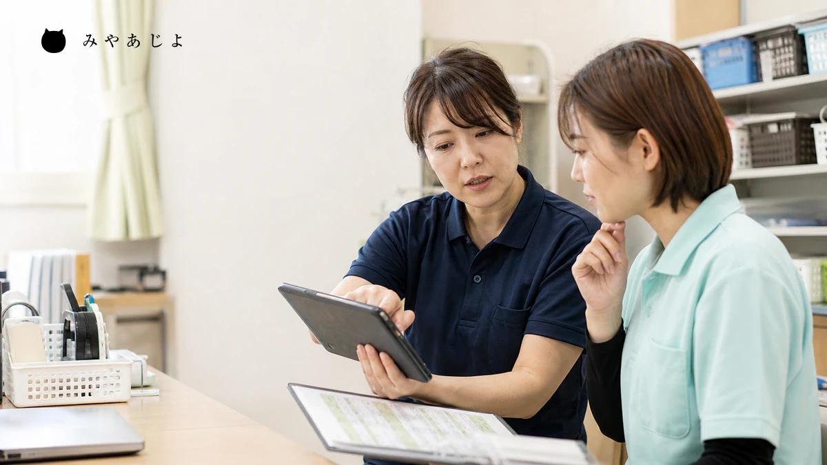 介護事業所で先輩職員が新任職員に記録方法と一日の流れを説明するイメージ