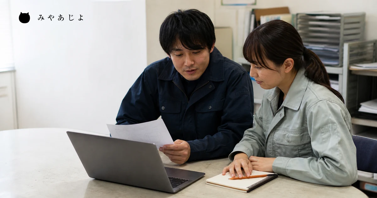 担当者が更新依頼票とノートパソコンを見ながら作業方法を相談する場面