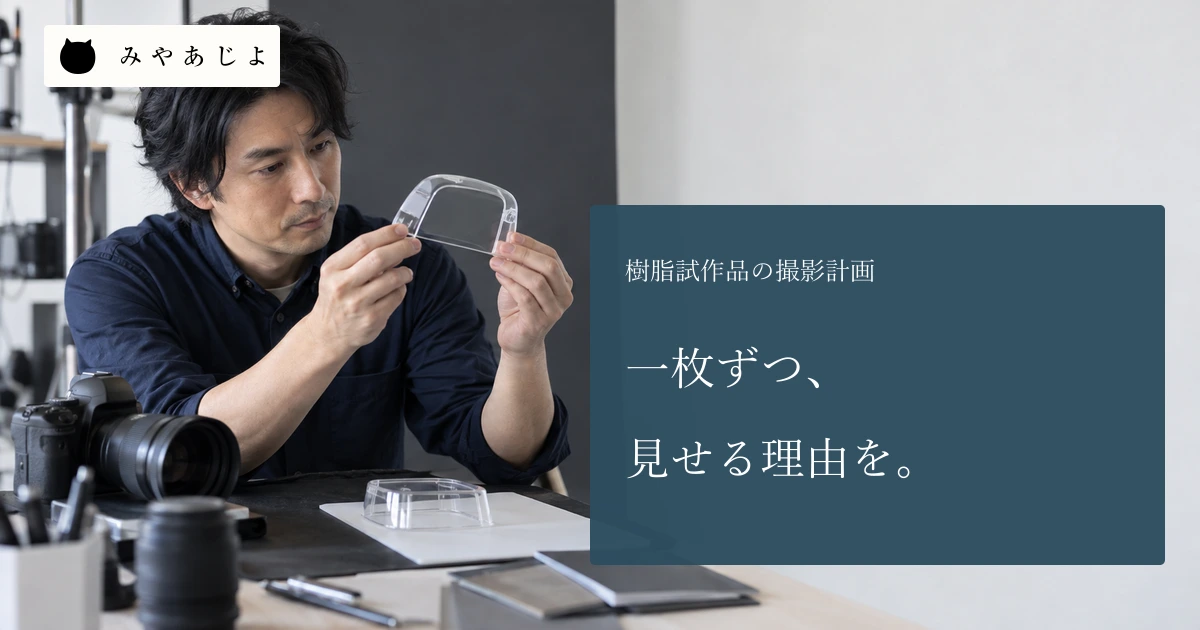 成人担当者が無記名の透明カバー模型を撮影台で確認する場面