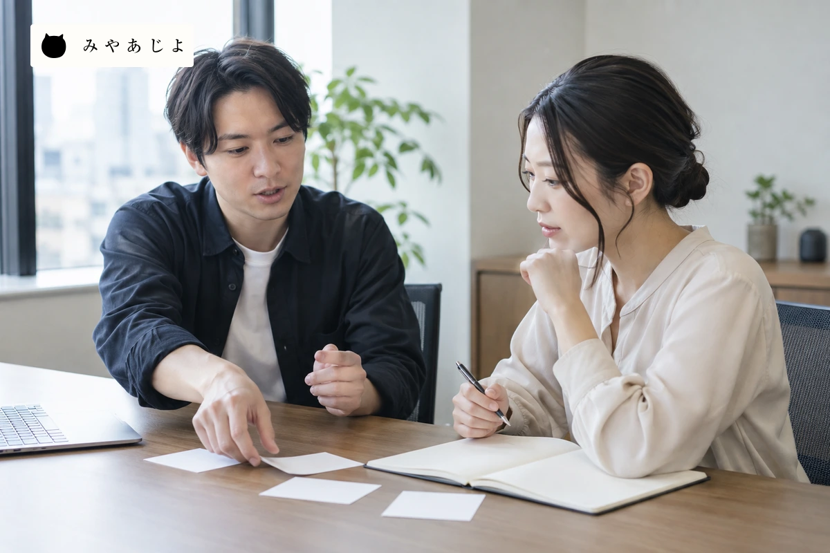 成人開発担当者二人が無記名の工程カードと空白のノートを見ながら相談範囲を確認する場面