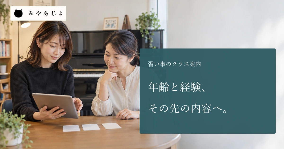 音楽教室の成人担当者二人が無記名のクラス案内を教室内で確認している場面