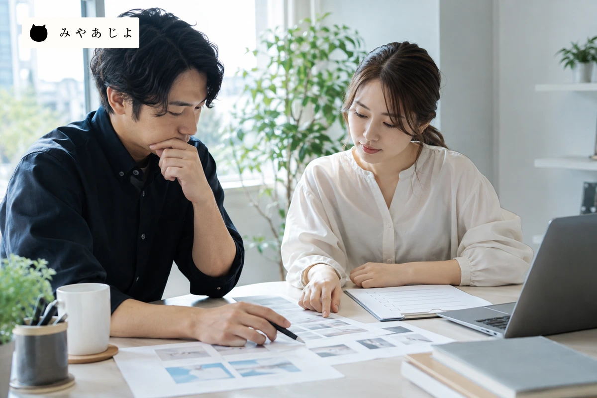 制作担当者が三者の作業範囲と無記名の画面資料を机上で確認する場面