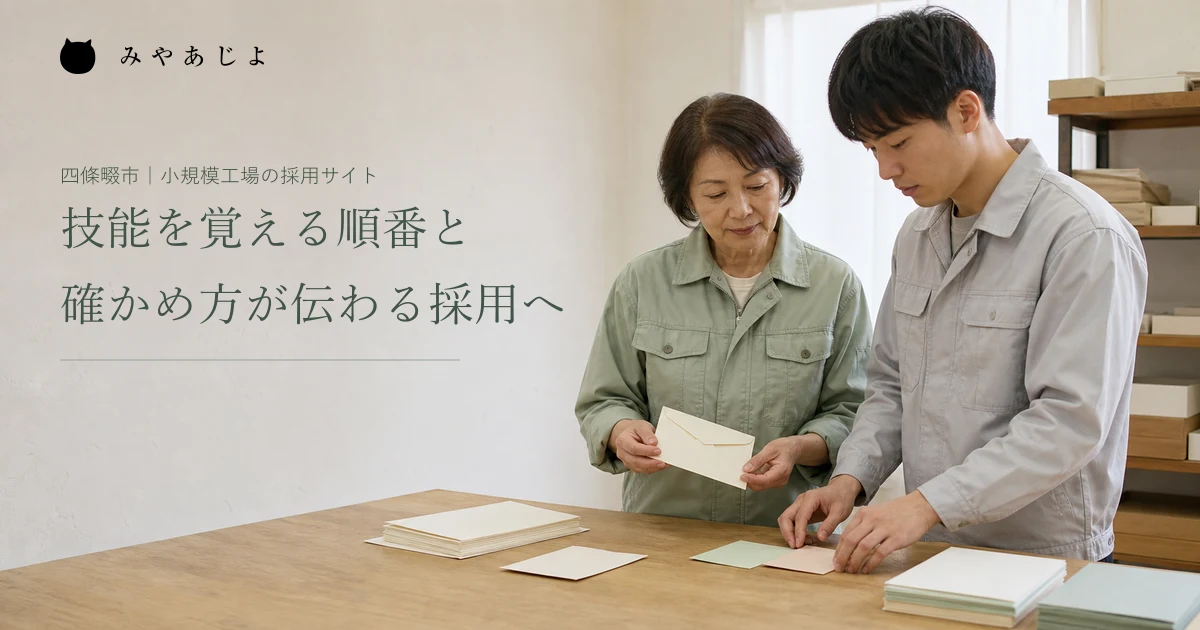 架空の紙製品工場で指導役と新人が机上の見本を確認しながら学ぶ編集イメージ
