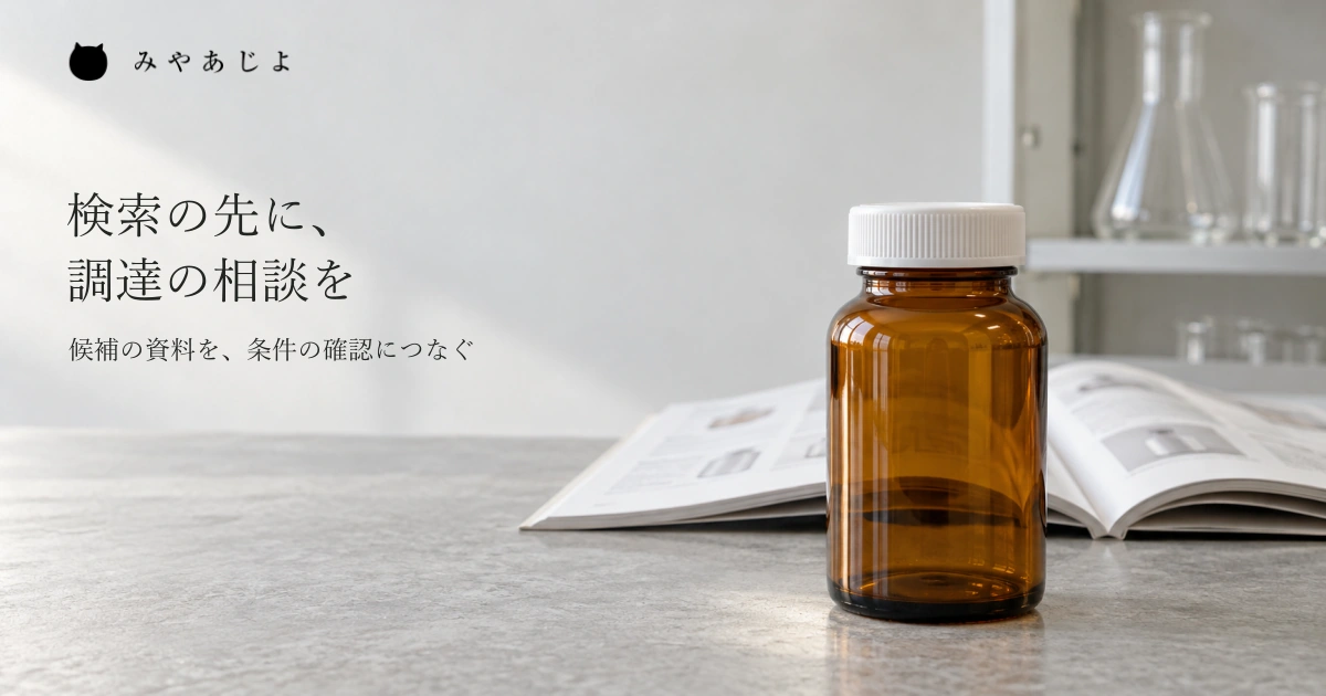 研究用品の商社の仕事場を想定し、閉じた無地の茶色いガラス容器と開いたカタログを近くで見せ、未掲載品の候補資料から調達相談を考える自然な写真イメージ