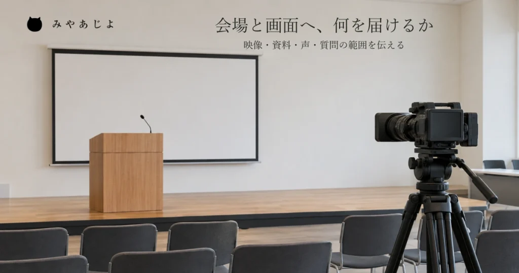 小さな催事会場で手前の業務用カメラが奥の演台とスクリーンへ向き、会場とオンラインへ届ける内容を考える自然な写真イメージ
