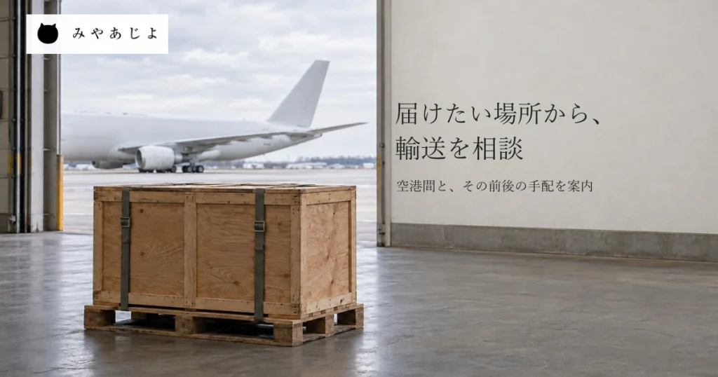 貨物ターミナルの内側から、左手前のパレットに載せた無地の木箱と屋外に停まる航空機を奥へ見通し、海外への輸送相談を想起する自然な写真イメージ