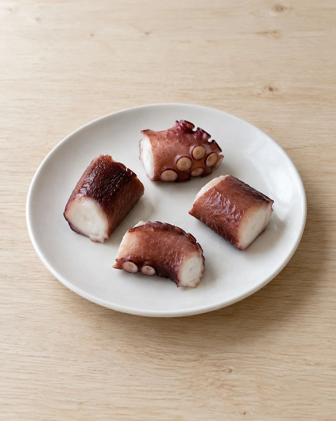 白い皿に並べたゆでたタコの切り身4片。加工食品の紹介を考えるための生成イメージ