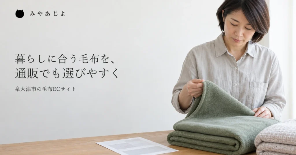 販売担当者が畳んだ毛布の一端を持ち、質感を確かめる一般的な作業イメージ