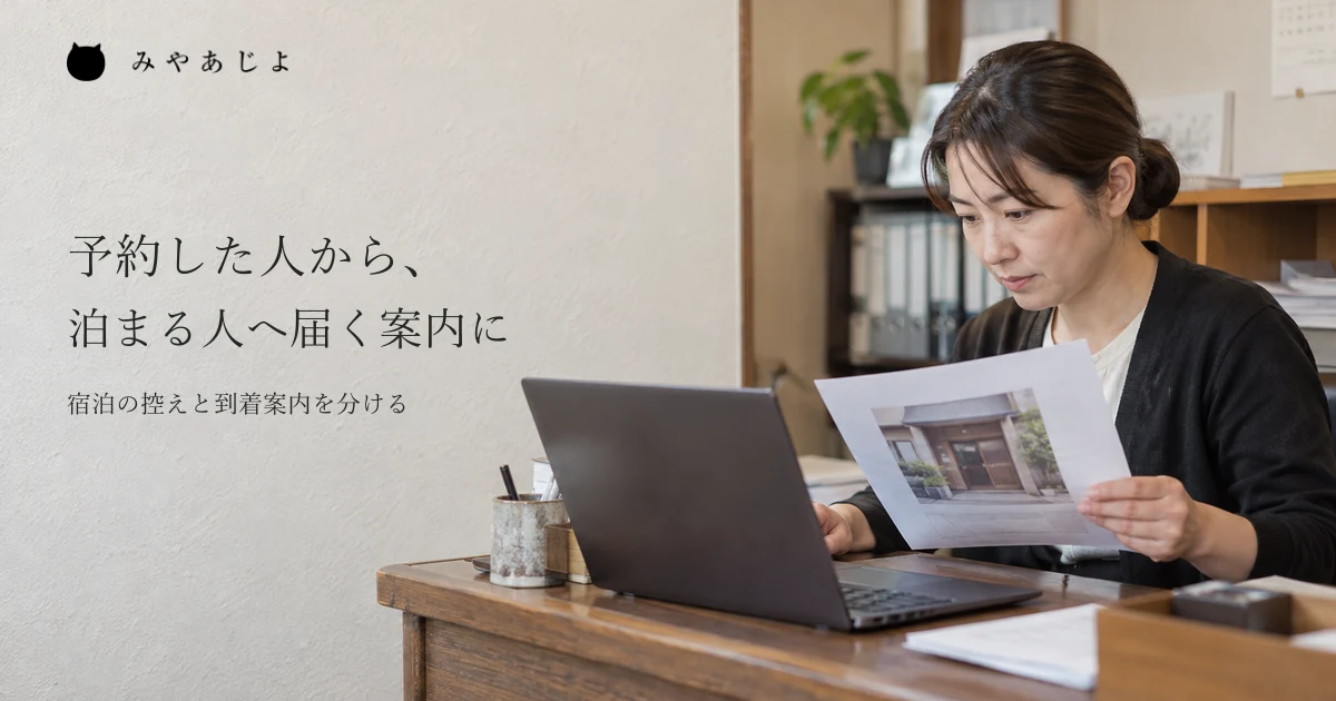 宿泊の控えと到着案内を机で見直す、宿の担当者のイメージ